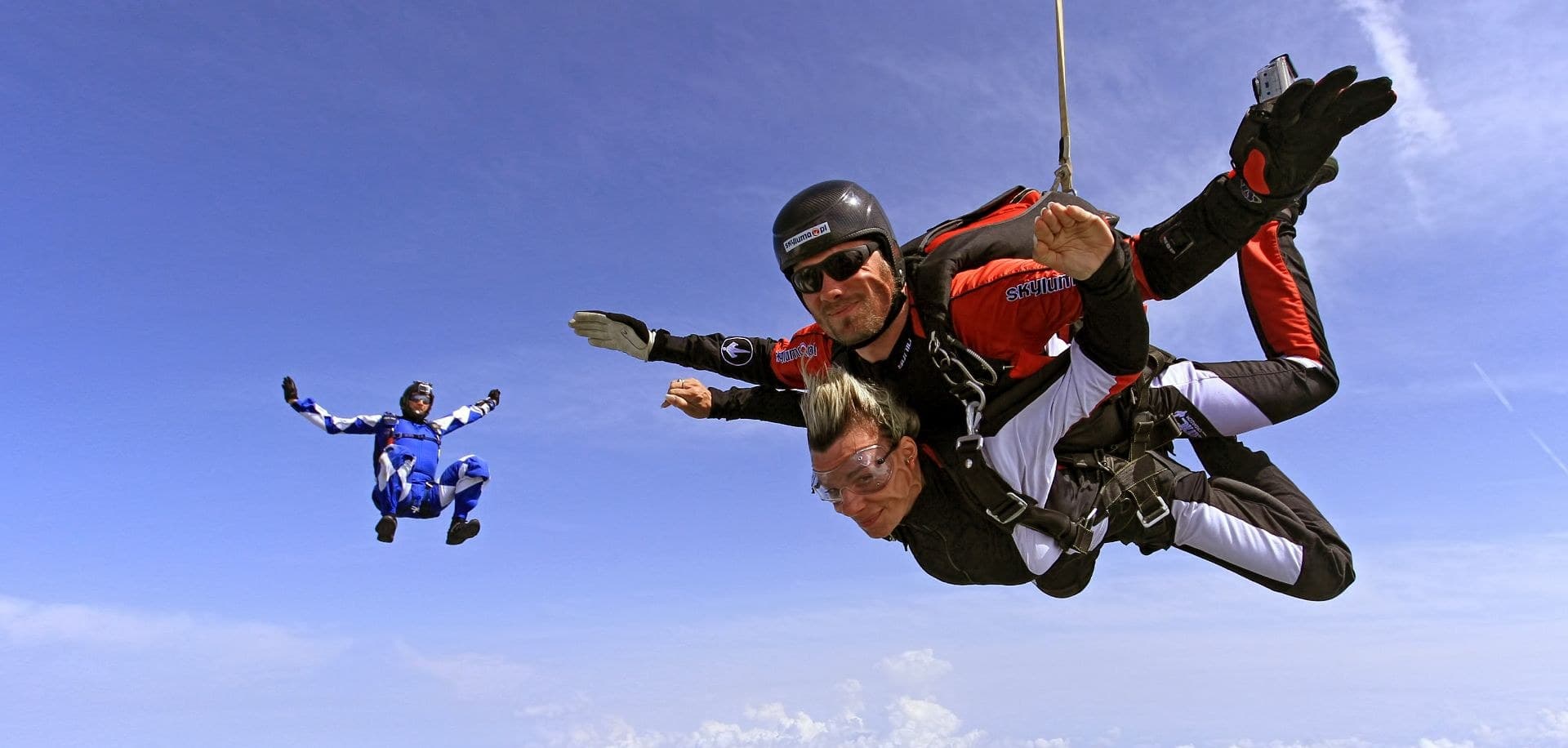 A tandem in freefall with the camera flyer beside them, camera on his helmet