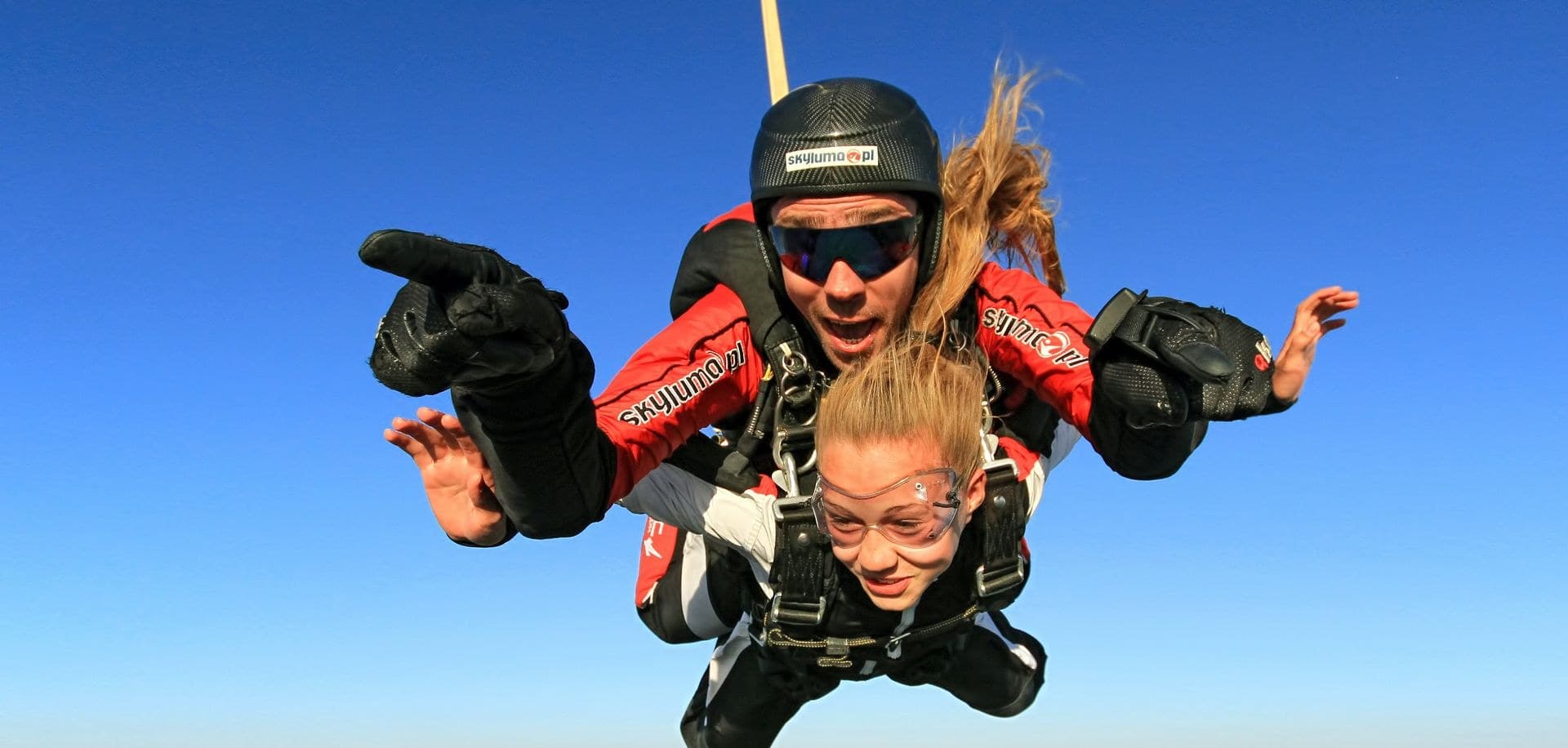 A tandem in freefall, hair streaming in the wind against a deep blue sky