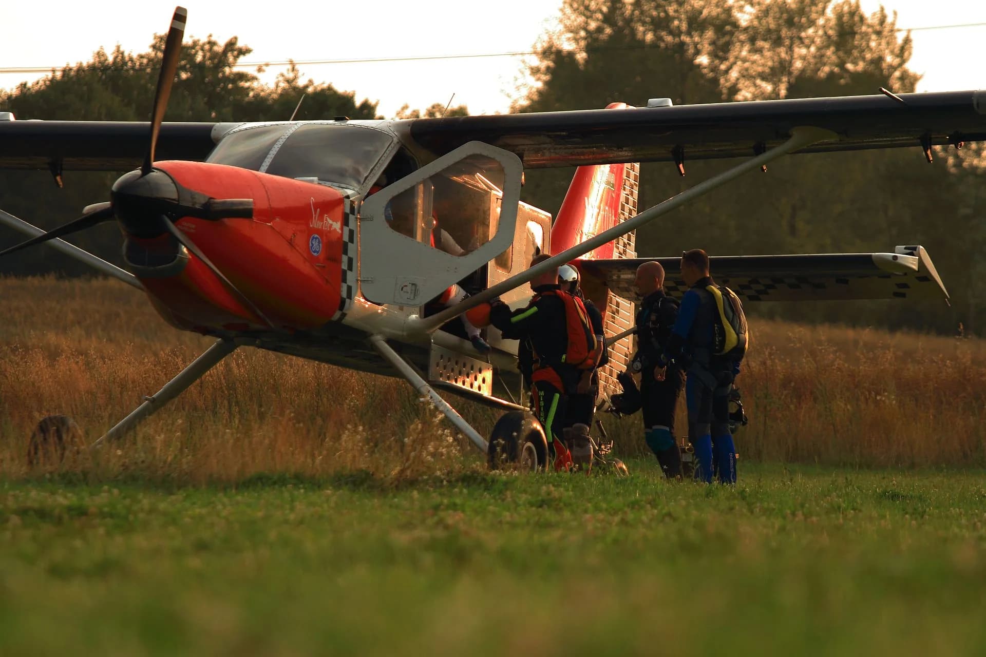 A red-and-white jump plane parked in tall grass in golden evening light