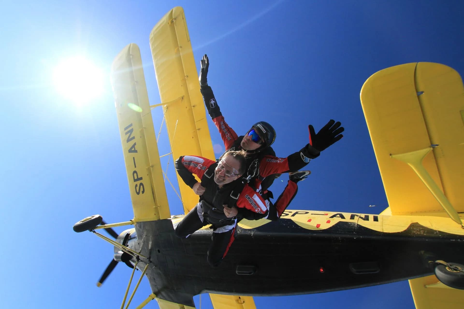 A tandem pair exits the yellow biplane straight into the sun