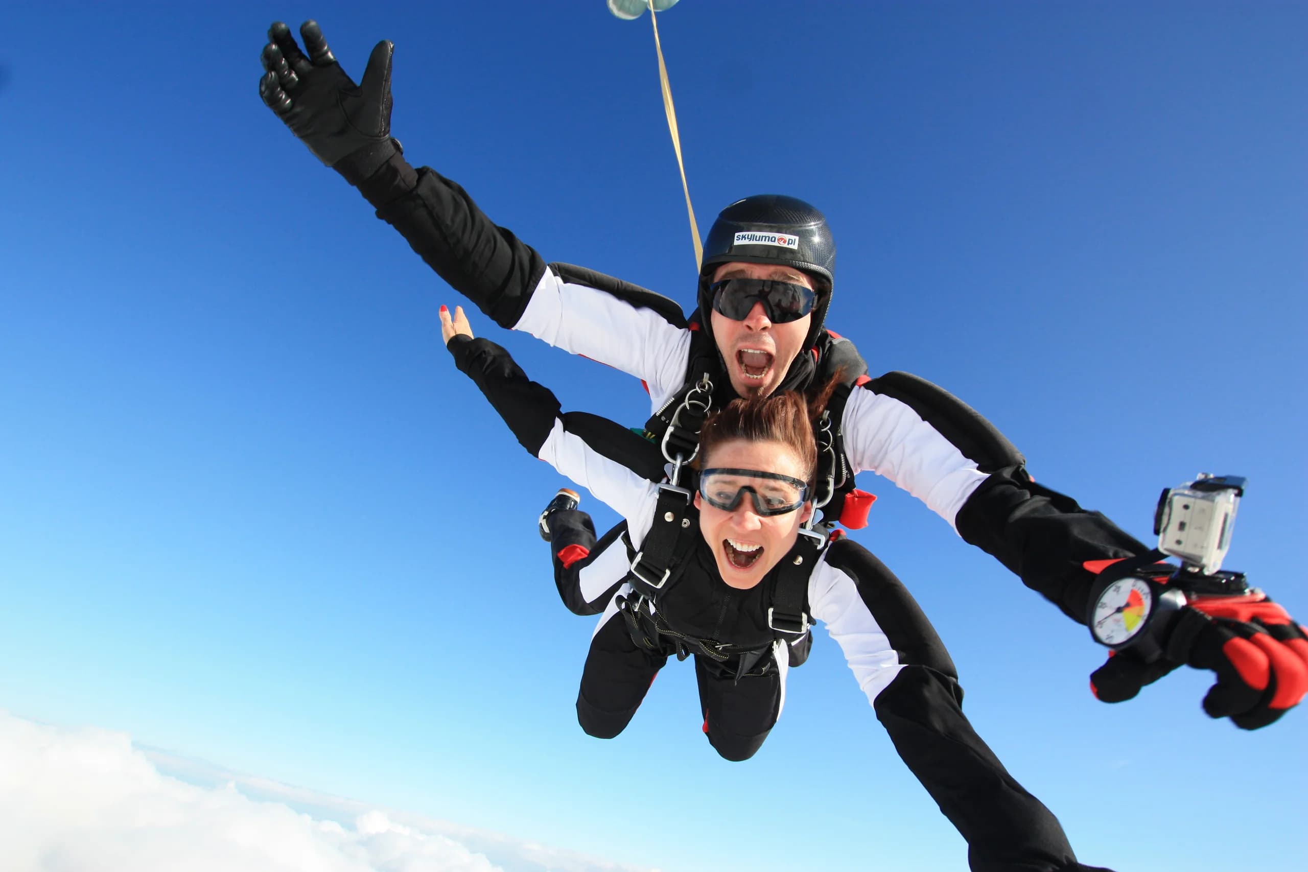A tandem pair in freefall high above the ground, arms wide