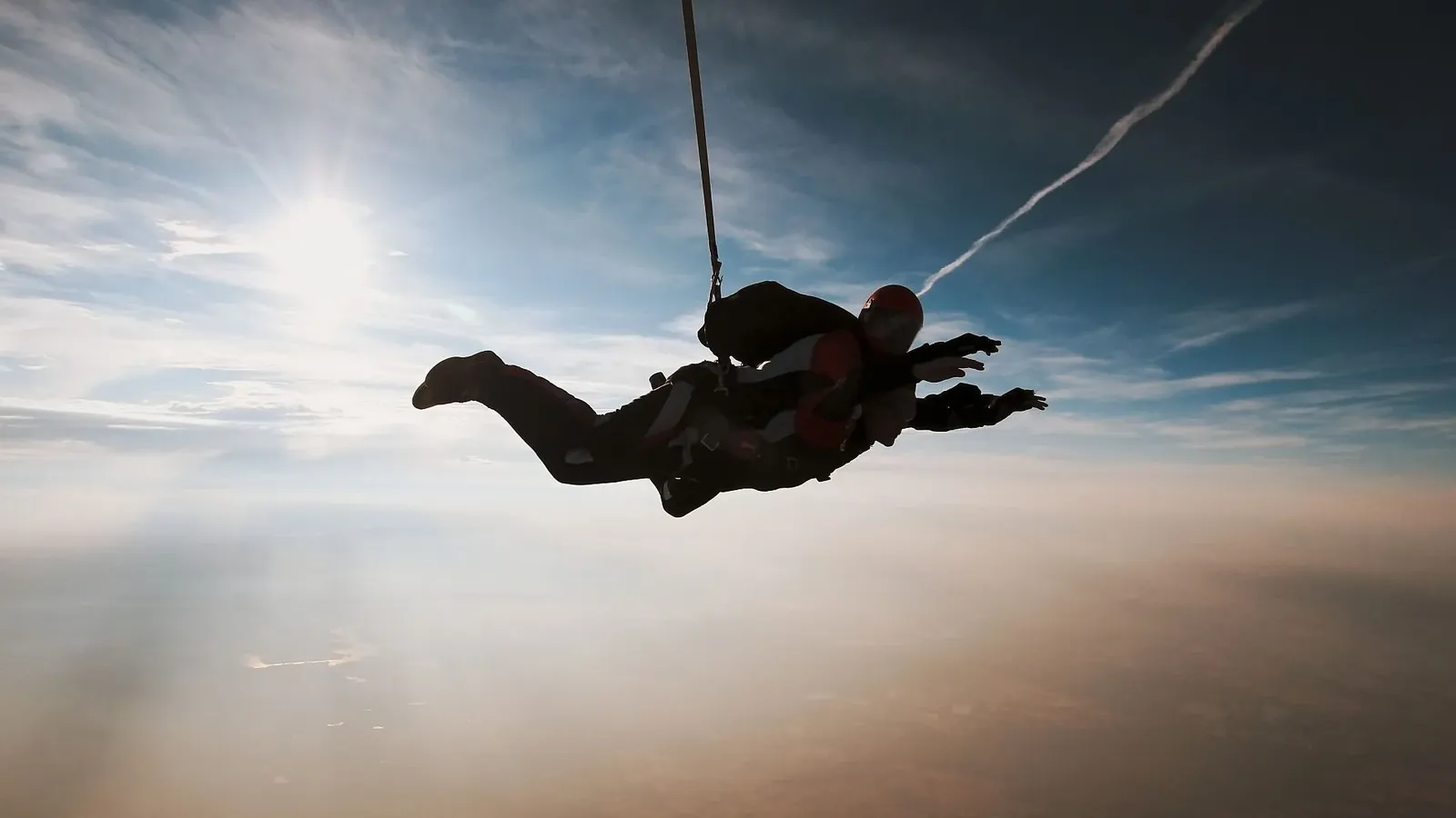 A tandem pair in freefall, silhouetted against the sun